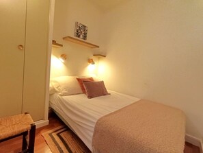 Et lille, hyggeligt soveværelse med en enkeltseng, en stol og et natbord.
