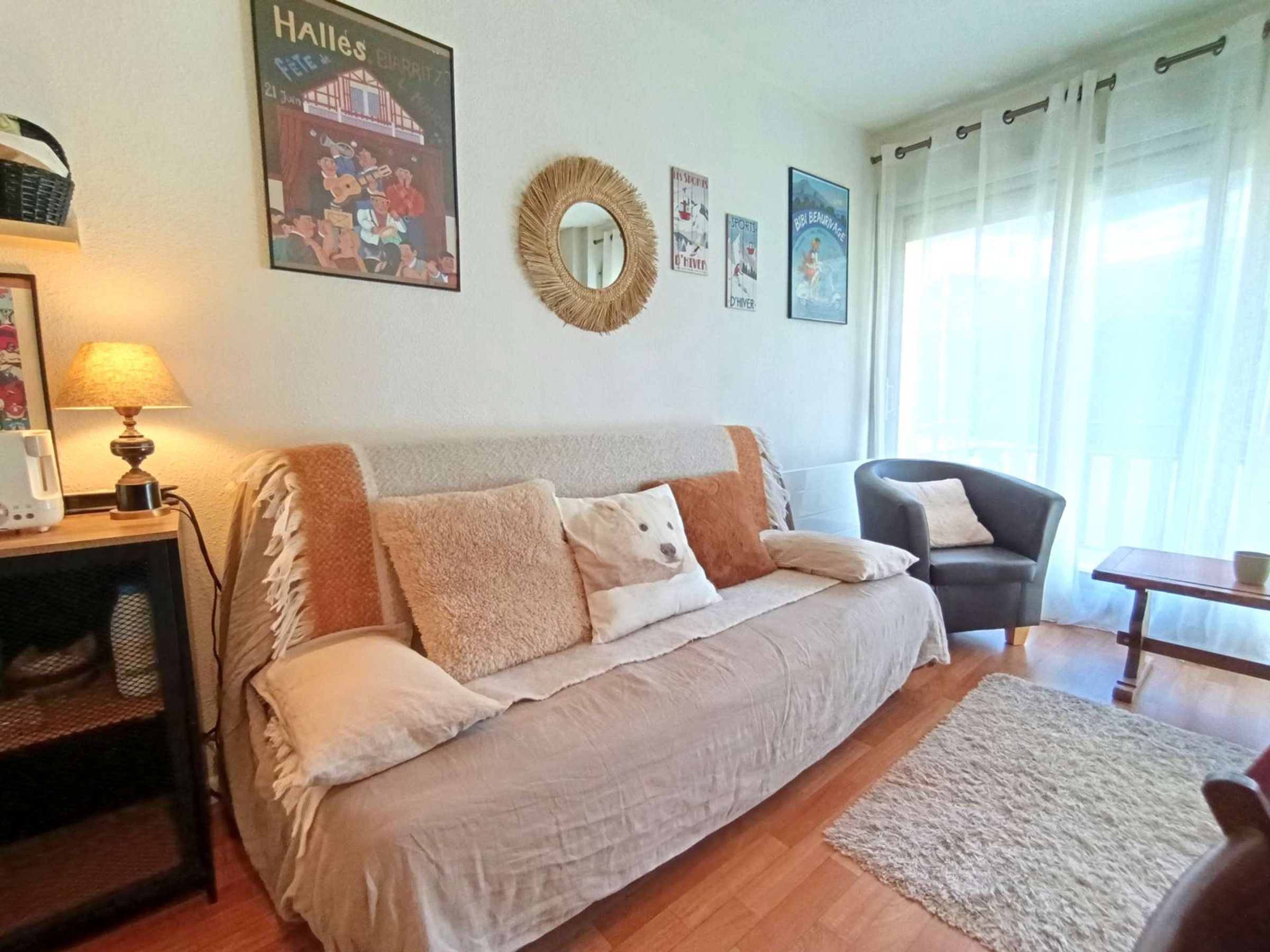 A cozy living room with a sofa, armchair, and a coffee table. There are wall decorations and a lamp on a side table.