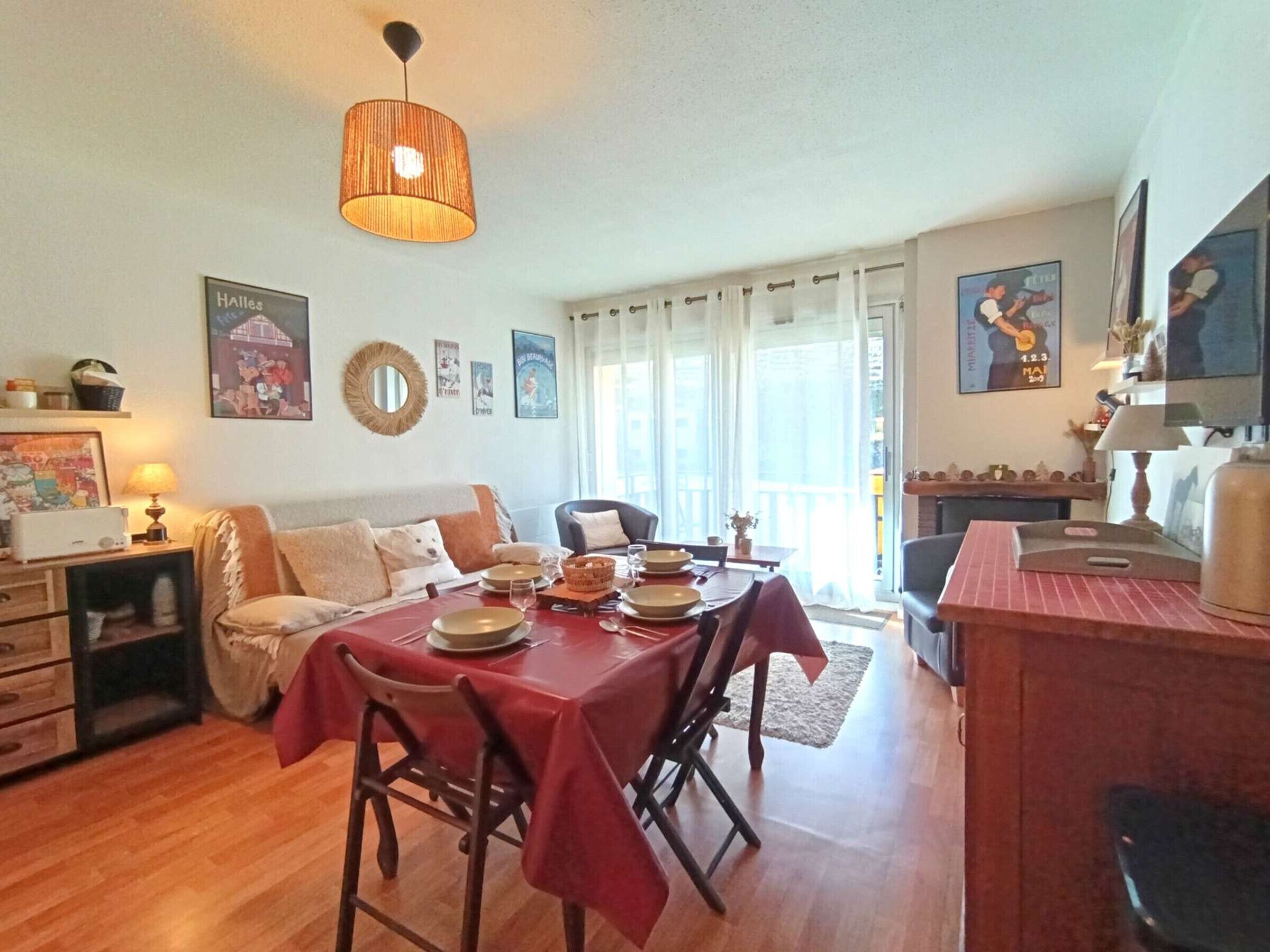 Een eetgedeelte met een tafel voor vier personen, een bank, een kitchenette en een balkon met gordijnen.