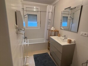 A small, modern bathroom with a bathtub, a sink, a mirror, and a window.