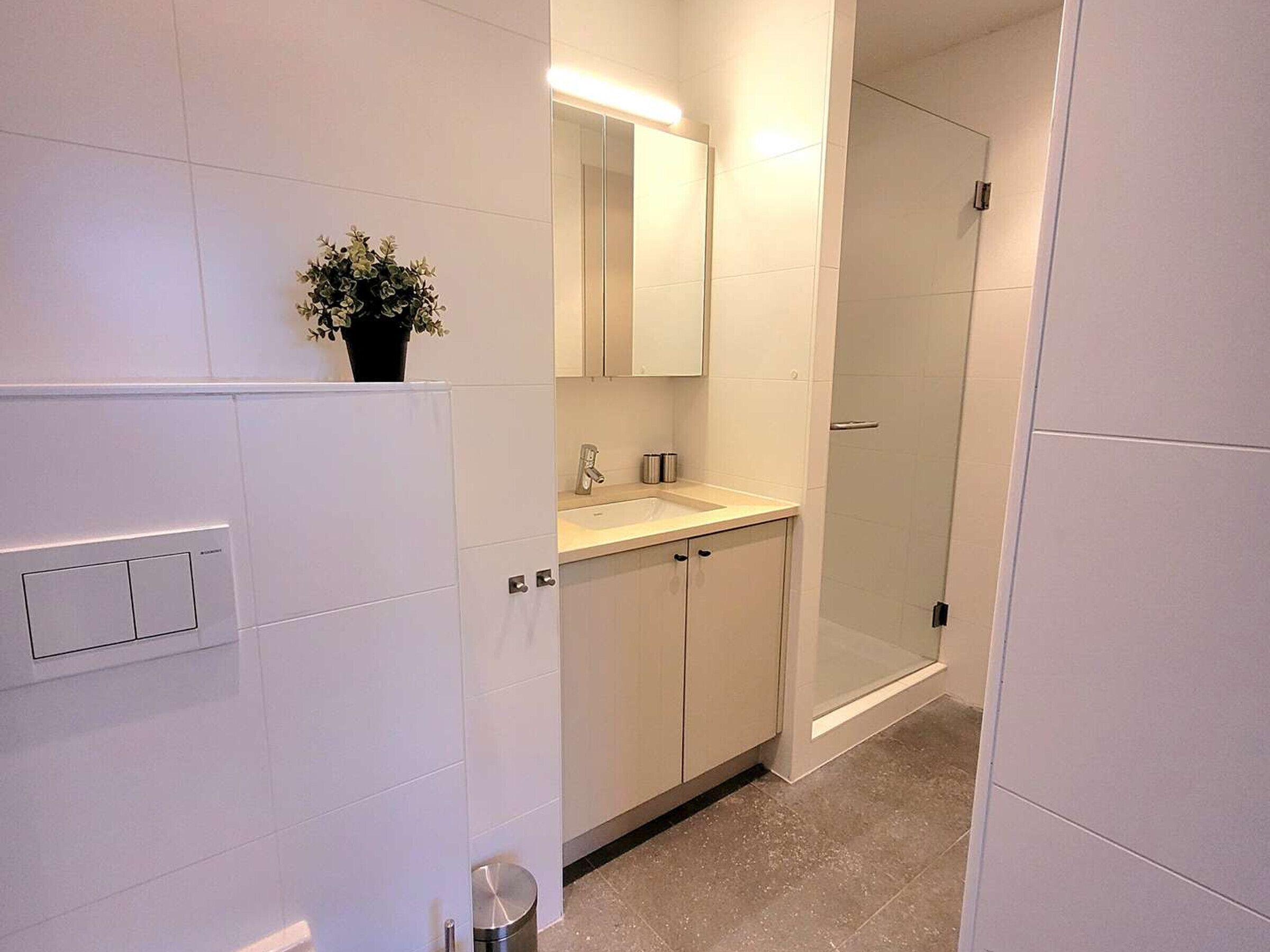 Een moderne badkamer met witte tegels, een wastafel, een spiegel en een douchecabine.