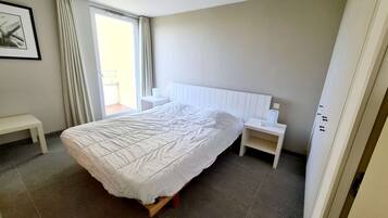 Een slaapkamer met een groot bed, een nachtkastje, een bankje en een raam met gordijnen.