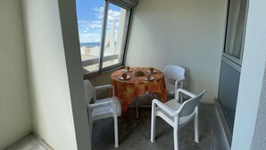 Un petit balcon avec une table et des chaises, une vue sur la plage et un mur blanc.