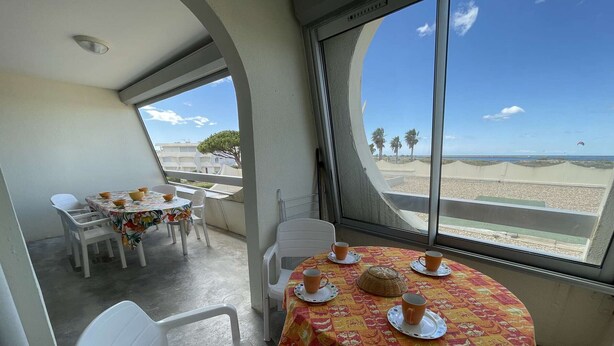 Un balcon avec une table dressée pour deux personnes, donnant sur une plage.