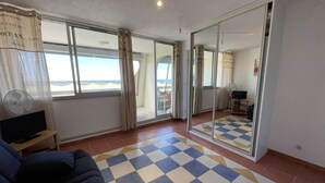 Une pièce dotée d’une grande porte-fenêtre coulissante donnant sur un balcon, d’un sol à carreaux, d’un canapé, d’une télévision et d’un ventilateur.