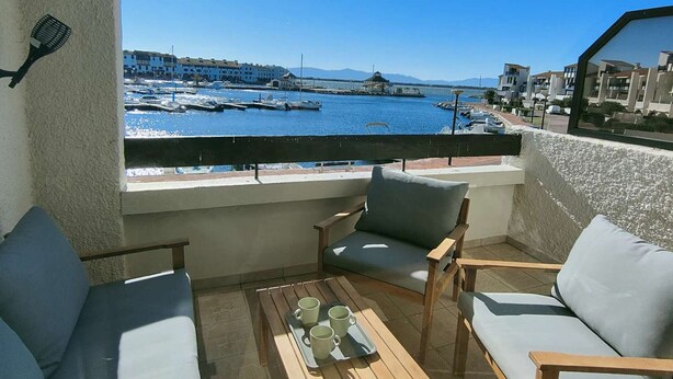 A balcony with a view of a marina, outdoor seating, and a cityscape in the background. - Charming T2 - 4 people - Terrace with port view (Le Barcarès)