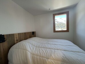 A bedroom with a wooden headboard, a single bed, and a window with a view of a snowy landscape.