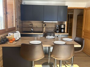 A modern kitchen with dark cabinets, a wooden countertop, a coffee maker, and a toaster. There are two chairs at a table set for two.