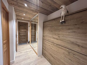 A hallway with wooden flooring and walls, a wooden ceiling, and a large mirror on one wall.