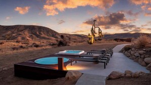 A desert landscape with a swimming pool, lounge chairs, and a hot tub.