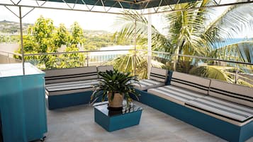 A balcony with a seating area, a potted plant, and a view of greenery and a body of water.