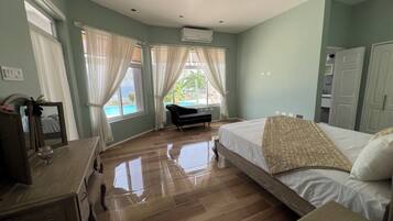Une chambre avec un plancher en bois, un lit avec une literie blanche, un canapé noir, un miroir et une fenêtre avec des rideaux.