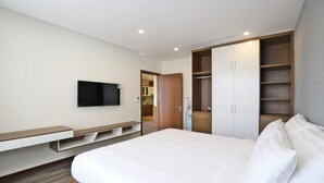 A modern hotel room with a large bed, a flat-screen TV mounted on the wall, a wooden wardrobe, and a built-in bench with storage. - Luxe Paradise Suites Tay Ho (Hanoi)
