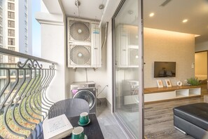 A modern apartment with a balcony, a washing machine, a dining area with a table and chairs, and a living room with a sofa and a TV. - Luxe Paradise Suites Tay Ho (Hanoi)