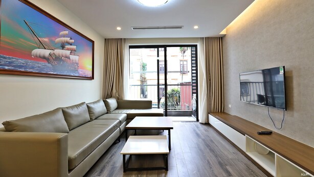 A modern living room with a sofa, a coffee table, a TV, and a painting of a ship on the wall. - Luxe Paradise Suites Tay Ho (Hanoi)