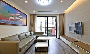 A modern living room with a sofa, a coffee table, a TV, and a painting of a ship on the wall. - Luxe Paradise Suites Tay Ho (Hanoi)