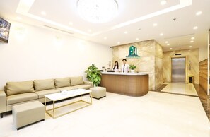 A modern hotel lobby with a reception desk, a sofa, a coffee table, and a reception area with two staff members. - Luxe Paradise Suites Tay Ho (Hanoi)