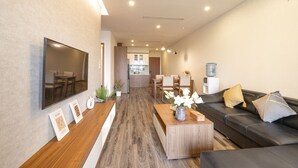 A modern living room with a flat-screen TV, wooden coffee table, and black leather sofa. - Luxe Paradise Suites Tay Ho (Hanoi)