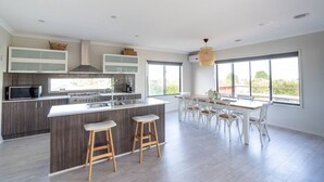 Una cocina moderna con una isla central, taburetes de bar y un comedor con sillas blancas.