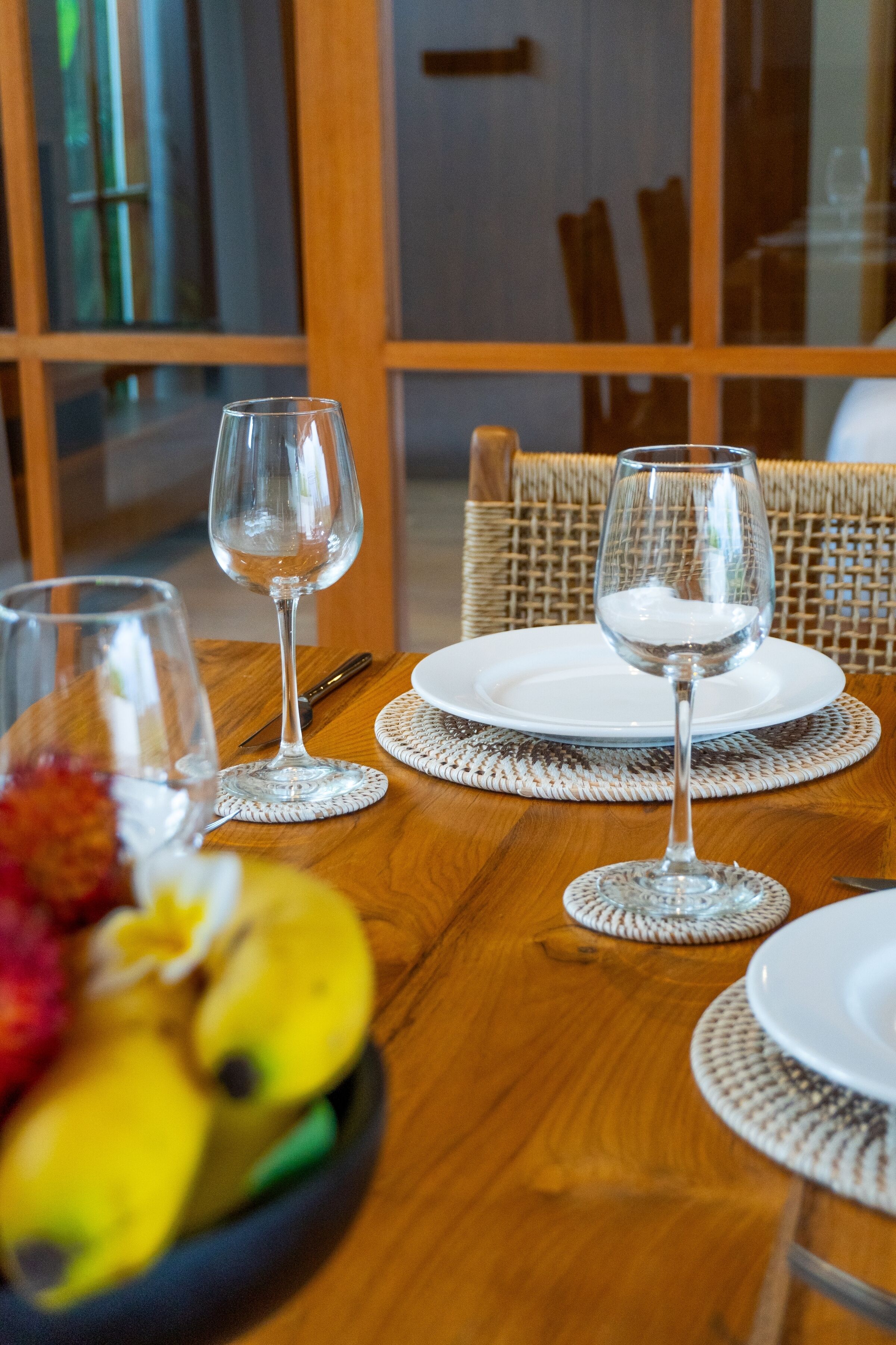 Una mesa de comedor dispuesta con copas de vino, platos y un frutero.