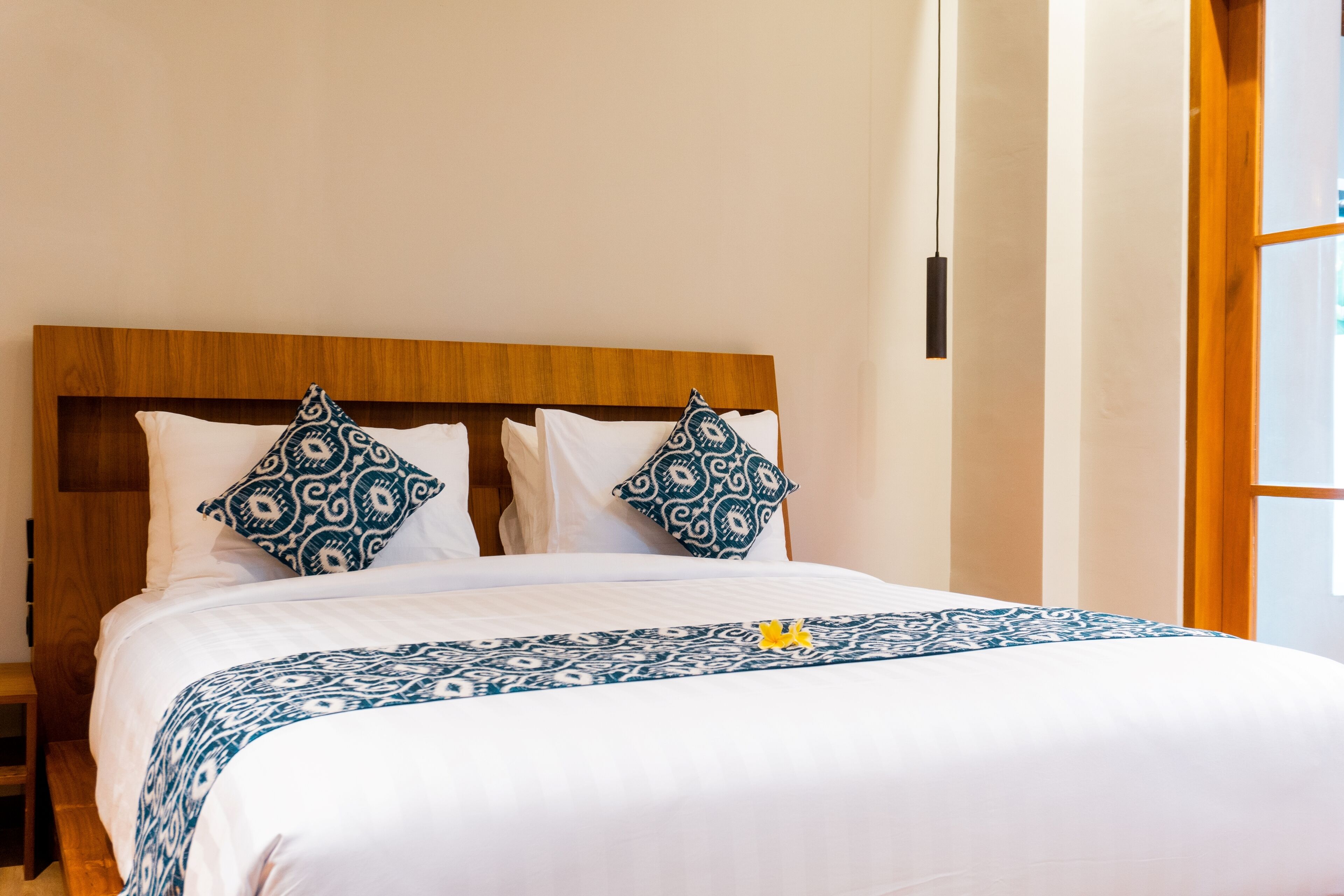 A neatly made bed with a patterned bedspread and two decorative pillows, a wooden headboard, and a bedside table.