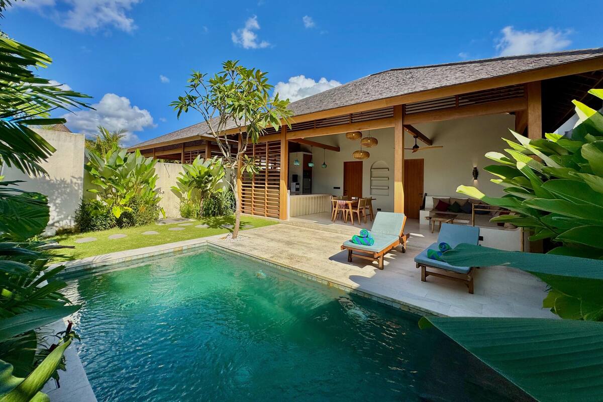 A modern house with a swimming pool, a dining area, and a patio with lounge chairs.