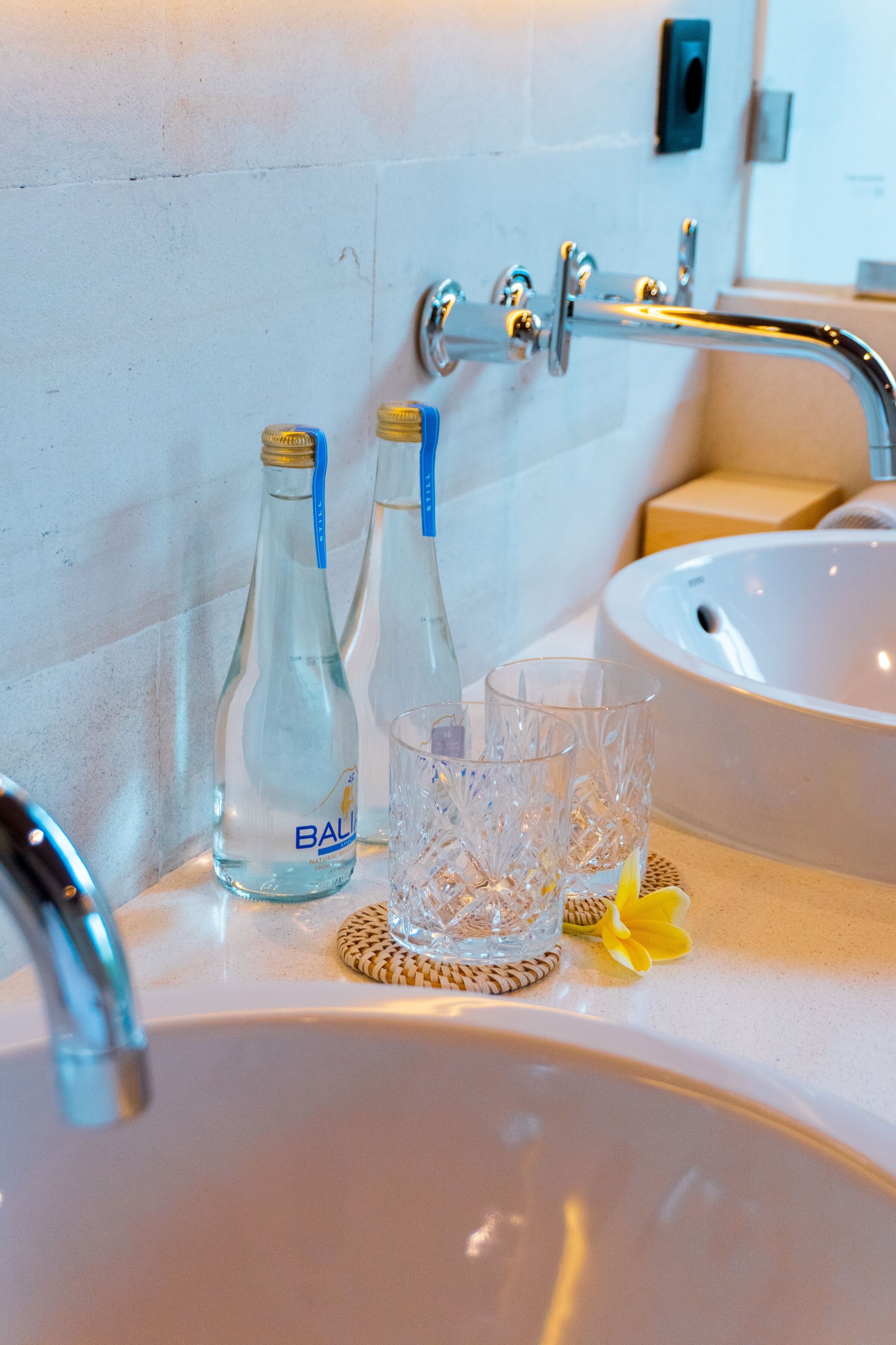 A bathroom sink with two bottles of Ball water and two clear glasses on a woven mat.