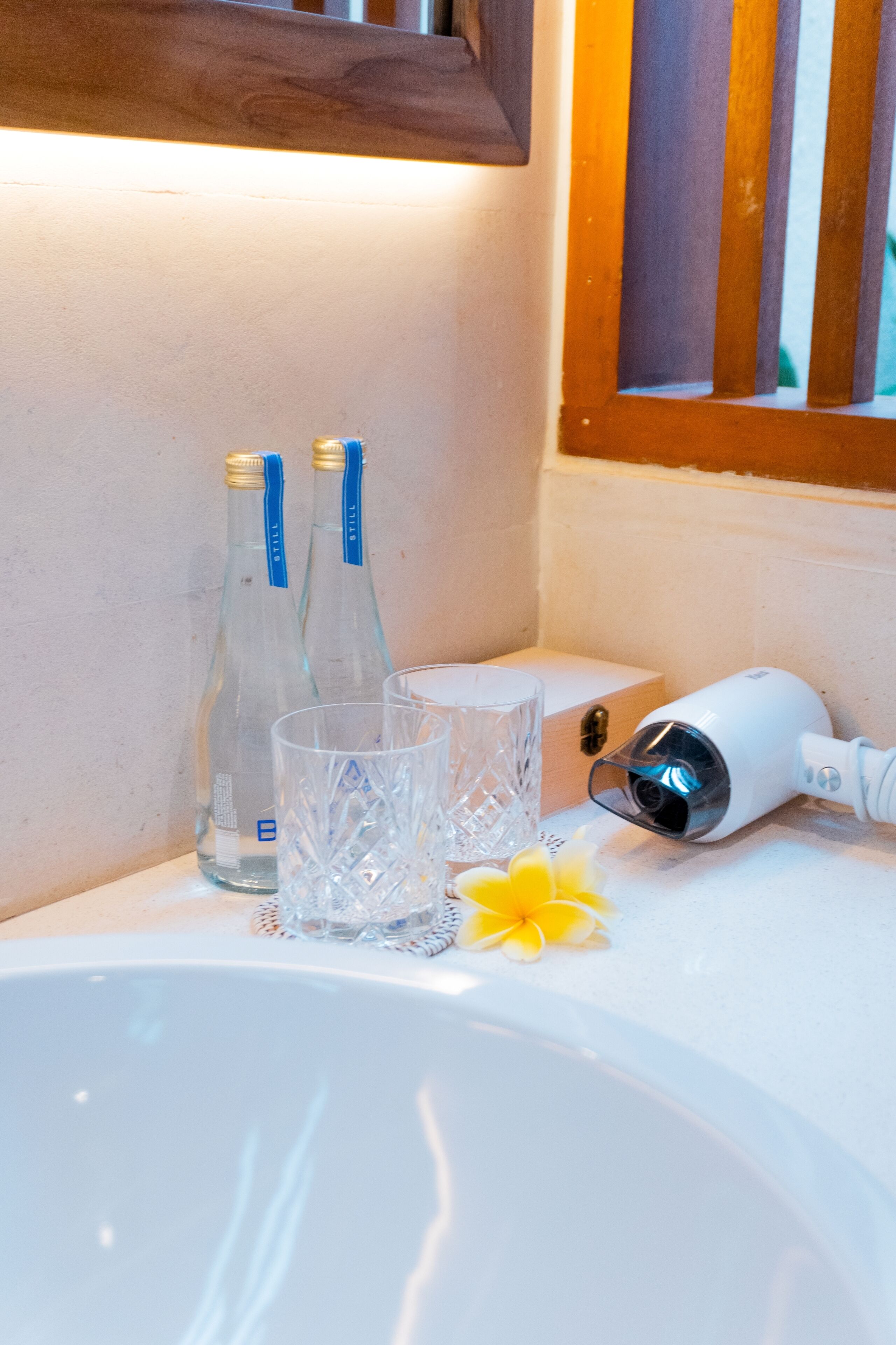 Ein Waschbecken mit zwei klaren Flaschen, einem Glas und einem Haartrockner auf einer weißen Arbeitsplatte.