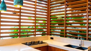Une cuisine moderne dotée d’un îlot central, de stores en bois à lames horizontales et de luminaires suspendus.
