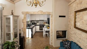 A living room with a blue sofa, a stone fireplace, and a kitchen in the background. - 3 bedroom stunning home in Zarace (Zarace)