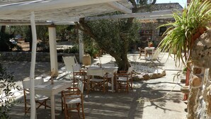 An outdoor patio with white tables and chairs, surrounded by stone walls and greenery. - MACCHIA SALENTINA small apartment 4 places in residence with swimming pool 2 km from the sea (Marina di Mancaversa)
