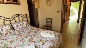 A bedroom with a floral bedspread, a chair, and a painting on the wall. - MACCHIA SALENTINA small apartment 4 places in residence with swimming pool 2 km from the sea (Marina di Mancaversa)