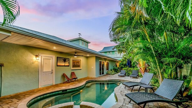 A swimming pool with a curved design, surrounded by lounge chairs and a patio area. - Cocktails and Dreams by Beach Boutique Rentals (Holmes Beach)