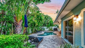 A backyard with a swimming pool, lounge chairs, and lush greenery. - Cocktails and Dreams by Beach Boutique Rentals (Holmes Beach)