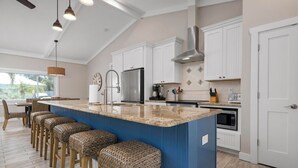 A modern kitchen with a large island, white cabinetry, and a blue accent wall. - Cocktails and Dreams by Beach Boutique Rentals (Holmes Beach)