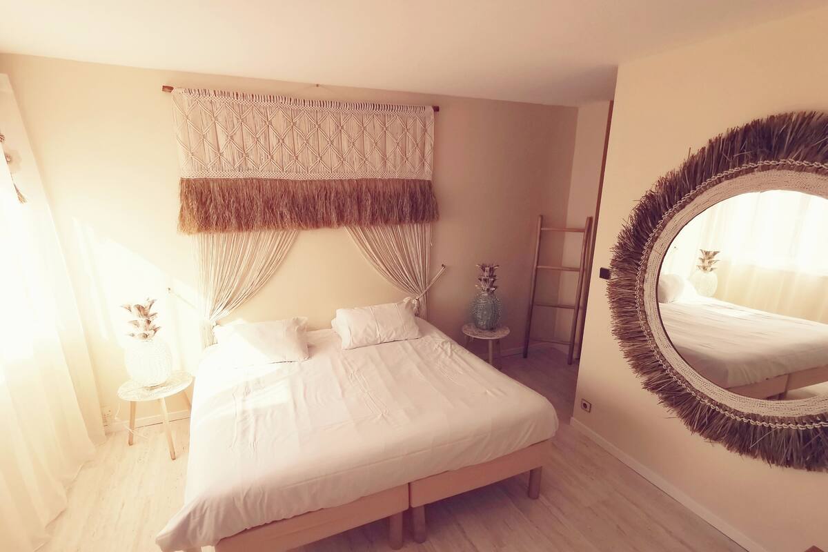 Una camera da letto con un letto, uno specchio tondo, un tavolino con un vaso e una scala appoggiata al muro.
