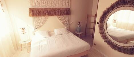 A bedroom with a bed, a round mirror, a small table with a vase, and a ladder against the wall.
