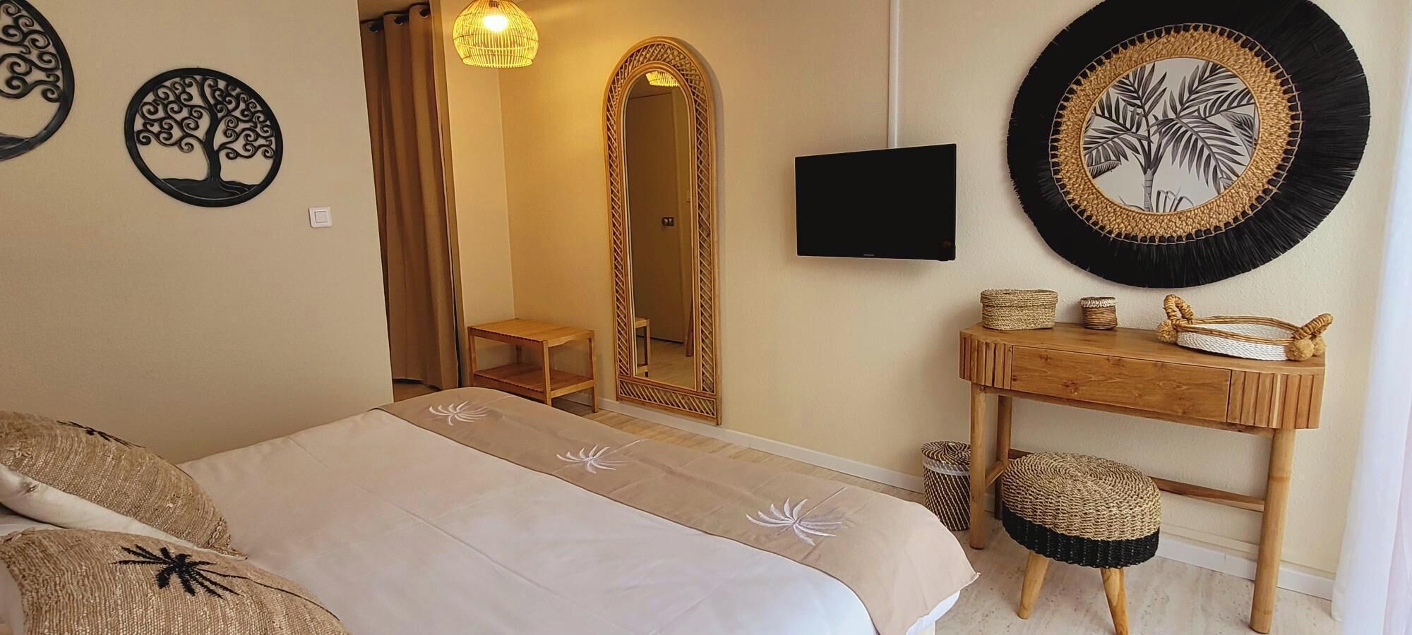 A bedroom with a bed, a wooden desk, a mirror, and decorative wall art.