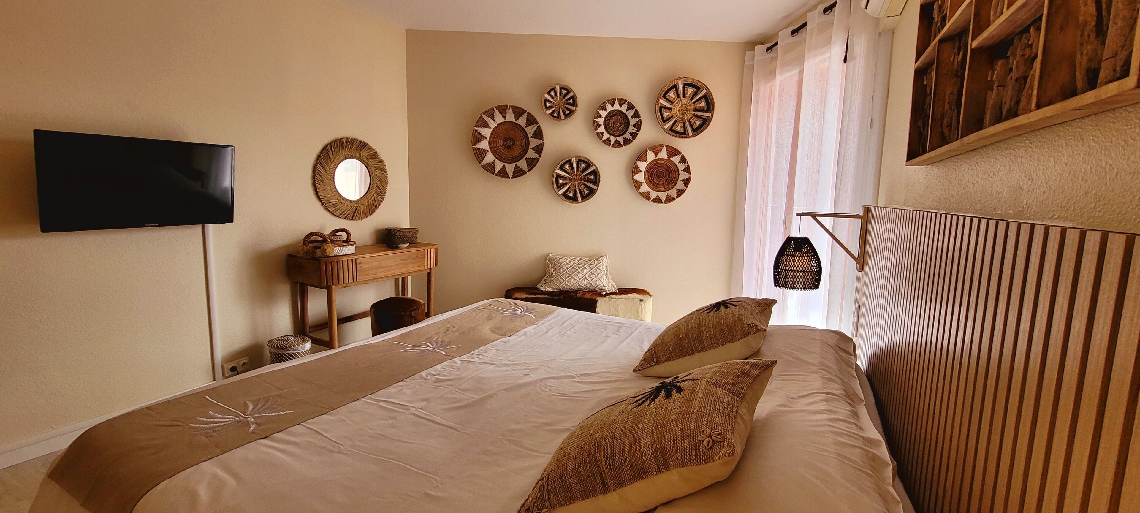 Une chambre à coucher comprenant un lit, un téléviseur fixé au mur, une commode en bois et des œuvres d’art décoratives accrochées au mur.