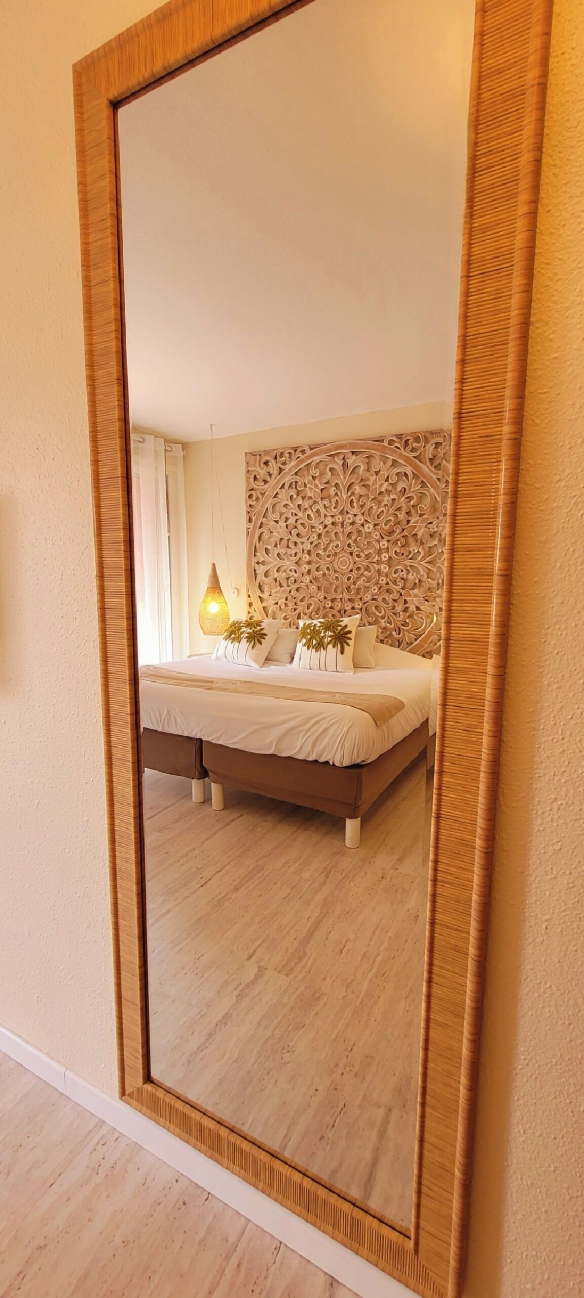 A bedroom with a large mirror, a bed, a decorative wall panel, and a bedside lamp.