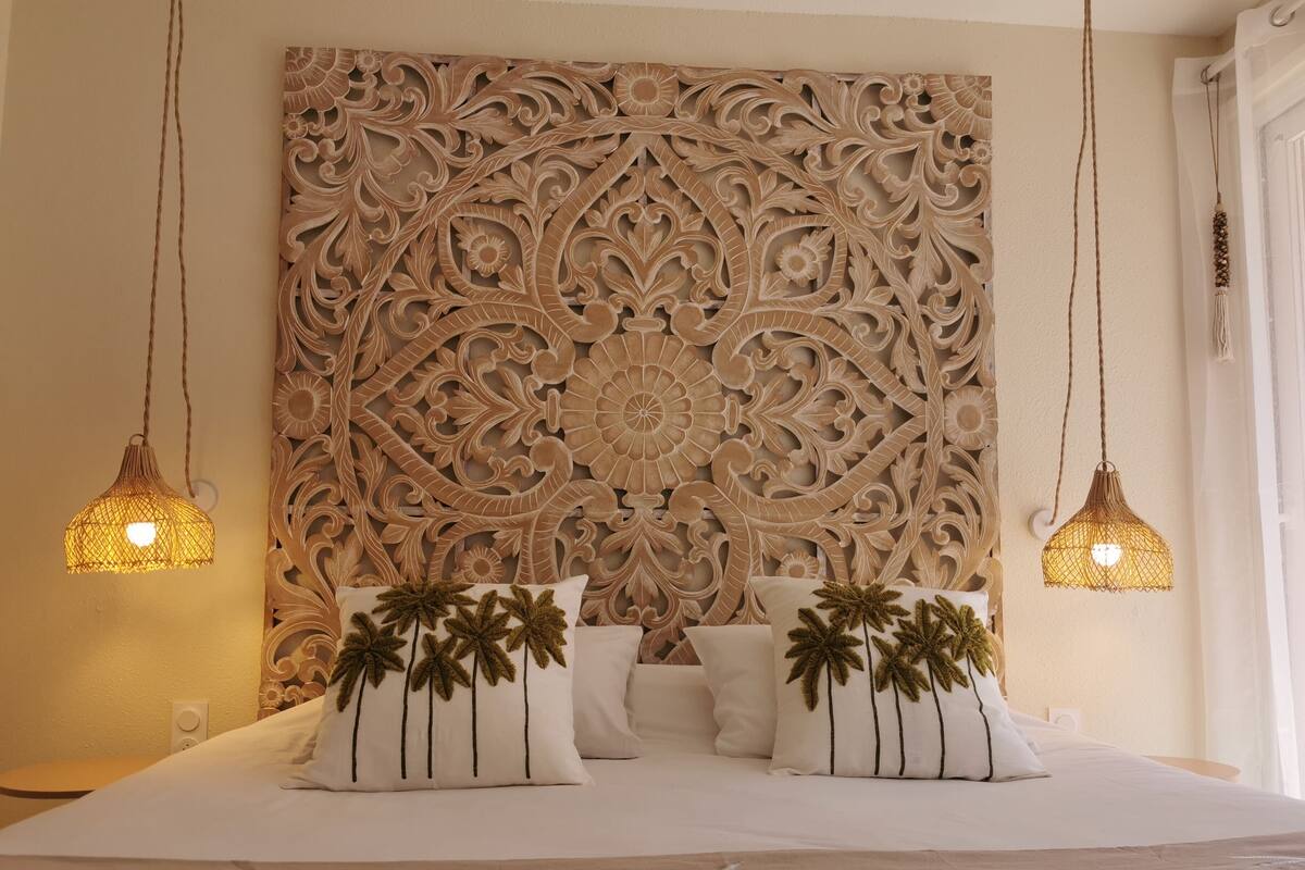 Un letto con una testiera decorativa, due lampade a sospensione e cuscini a forma di palma.