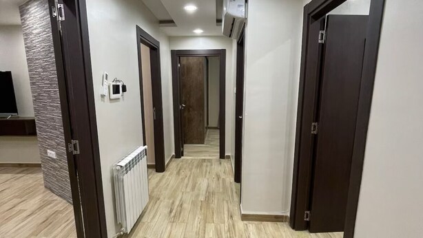 Un corridoio con pavimento in legno, pareti bianche e diverse porte.