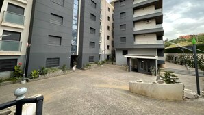 Un moderno edificio residenziale a più piani con balconi, un cortile pavimentato e alcune aree verdi.