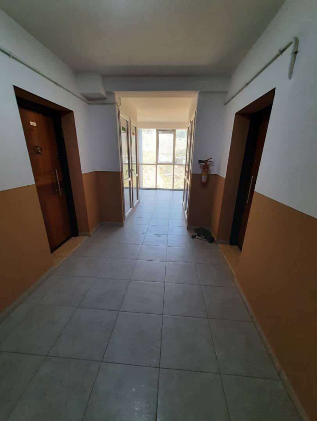 Un couloir bordé de portes des deux côtés, qui mène à un espace lumineux doté de fenêtres.