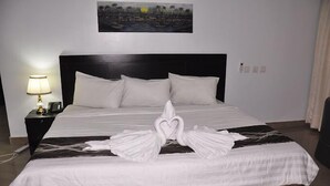 A hotel room with a large bed, a nightstand with a lamp, and a painting on the wall. - Aaliyah Royale Hotel  (Abuja)