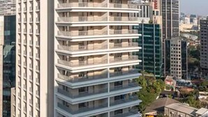 Un edificio alto con numerosi balconi, circondato da altri edifici e un cielo sereno.