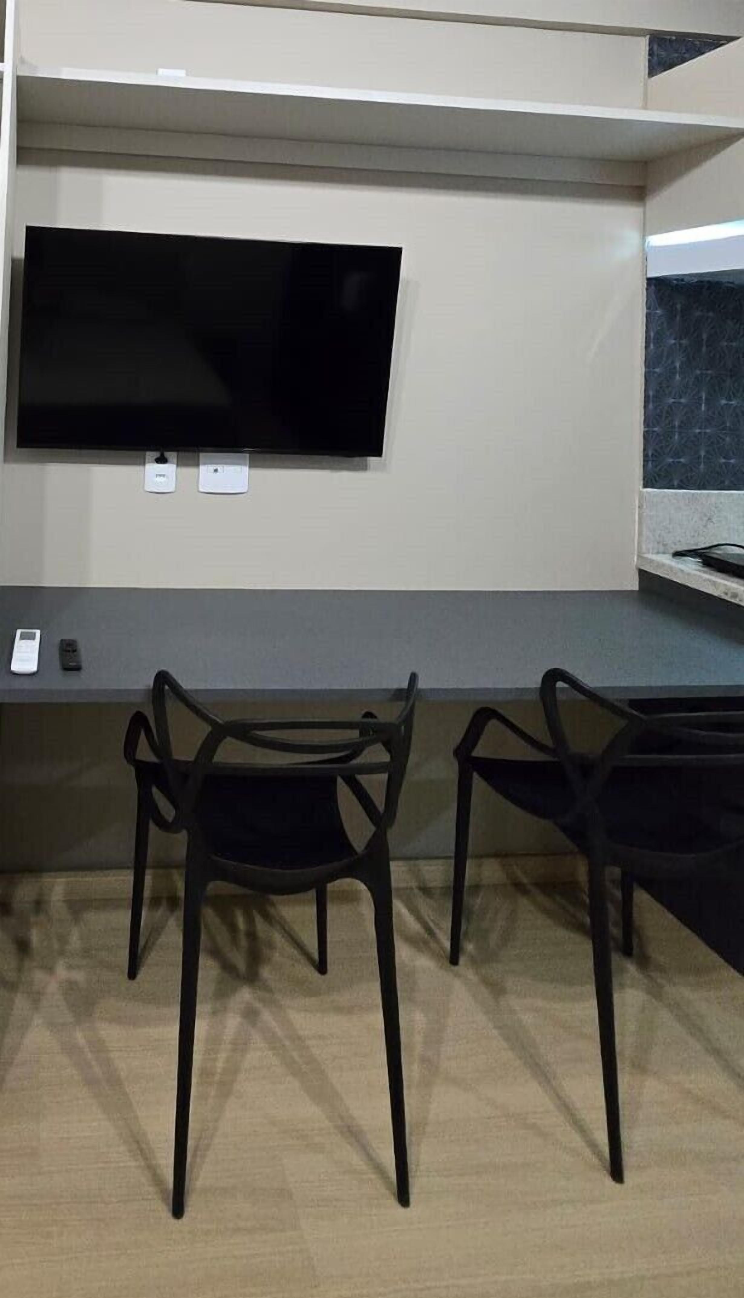 A room with a flat-screen TV mounted on the wall, two black chairs, and a small table.