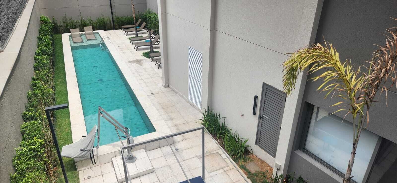 A rectangular swimming pool with a ladder, surrounded by lounge chairs and a small garden area.
