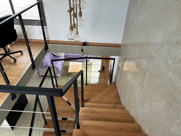 A staircase with wooden steps and metal railings, leading to a room with a bed and a desk.