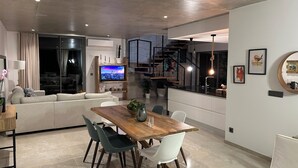 Un soggiorno moderno con divano, tavolo da pranzo e sedie, televisione e una scala che conduce a un piano superiore.